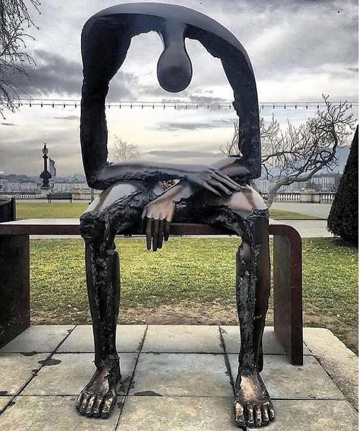A unique bronze street art sculpture of a figure sitting on a bench, head bowed. A stunning example of street art.