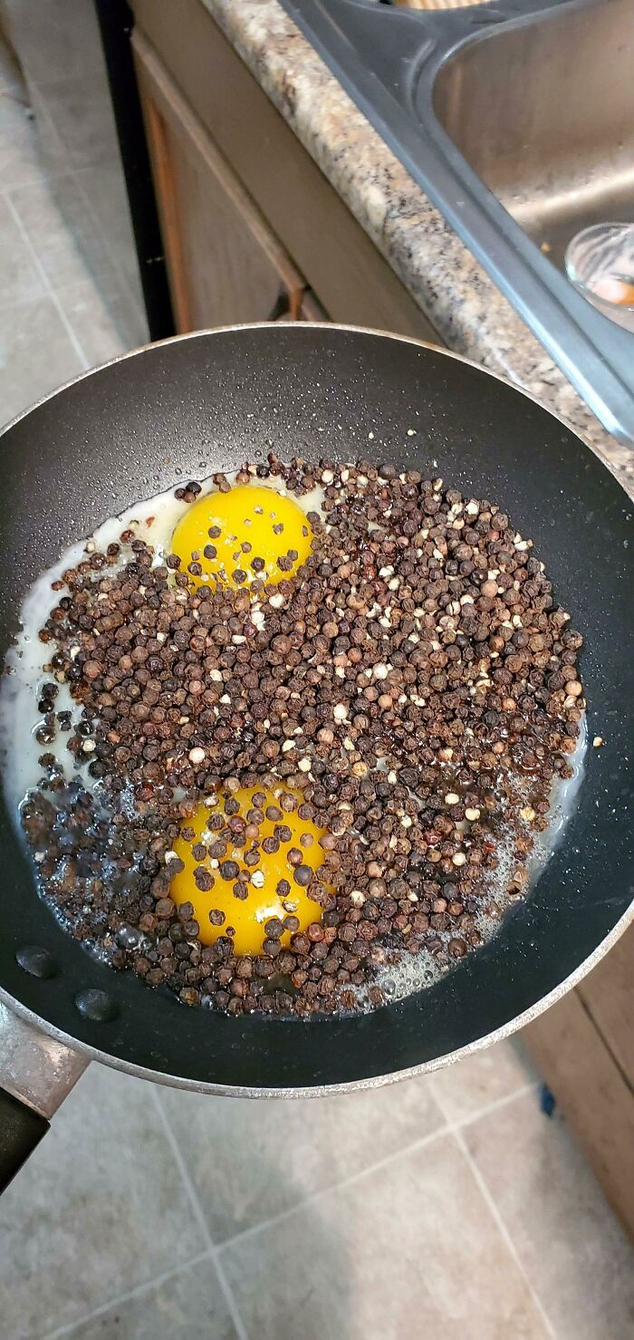 An unfortunate kitchen fail with two fried eggs covered in an excessive amount of black peppercorns in a frying pan.