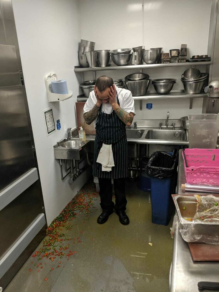 A distressed chef in a flooded kitchen, with peppers scattered on the floor, a severe kitchen fail.