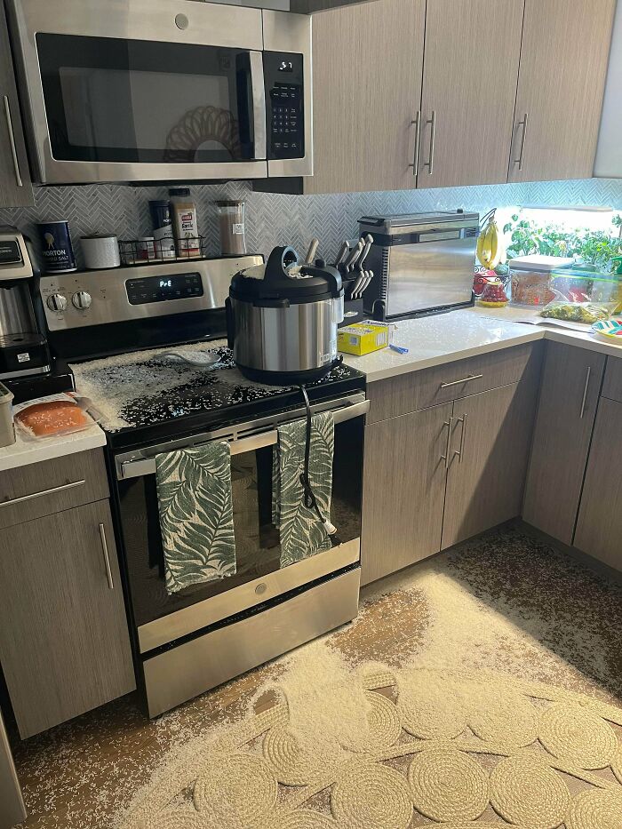 A modern kitchen with a large explosion of white contents on the stove, floor, and counters, a major kitchen fail.