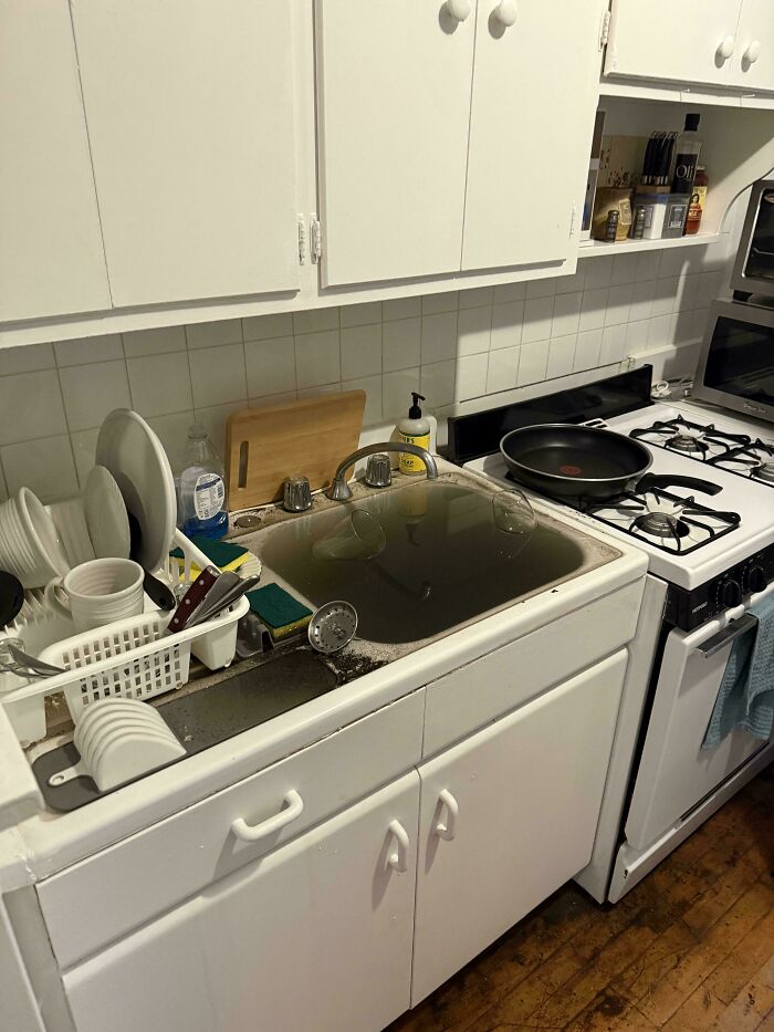 A dirty kitchen sink overflowing with water and piled with dishes, a clear kitchen fail.