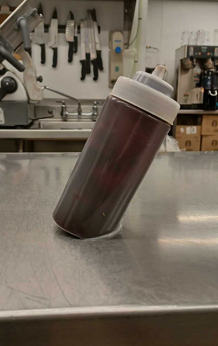 Squeeze bottle filled with dark liquid precariously balanced on a stainless steel counter, a kitchen fail waiting to happen.