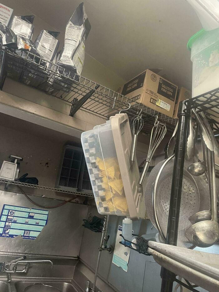 A cluttered commercial kitchen storage area with a container of chips hanging, illustrating kitchen fails.