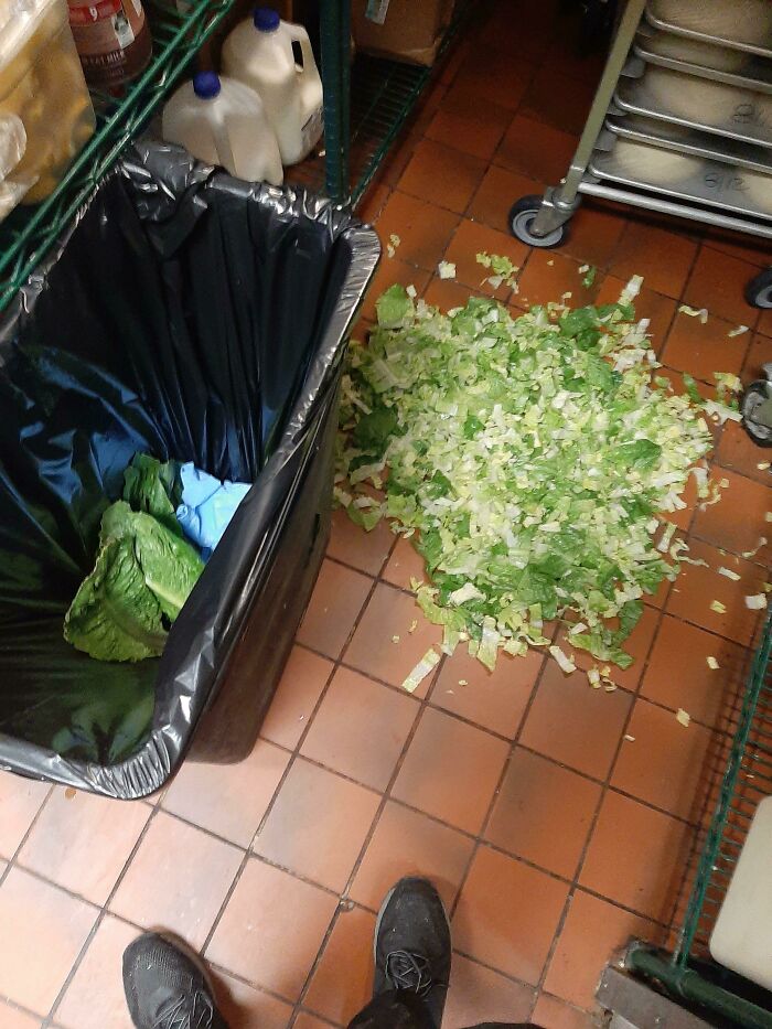 A pile of chopped lettuce on a tiled kitchen floor next to a trash can, an example of kitchen fails.