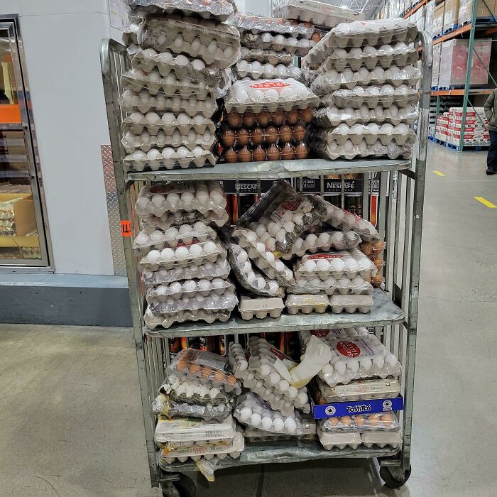 A rolling cart stacked high with numerous egg cartons, indicating a massive kitchen fail if dropped.