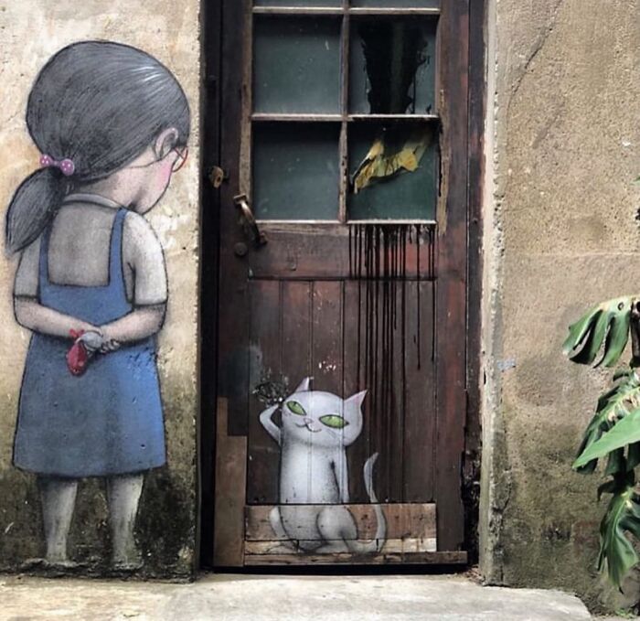 A charming street art piece featuring a girl and a cat painted on an old wall and door.