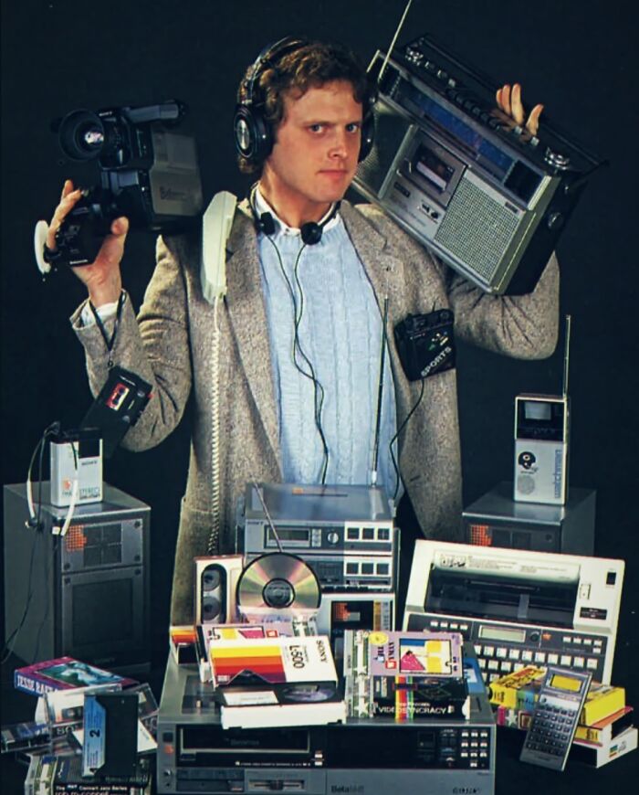 Retro tech photo of an 80s man surrounded by various gadgets, showcasing 80s technology.