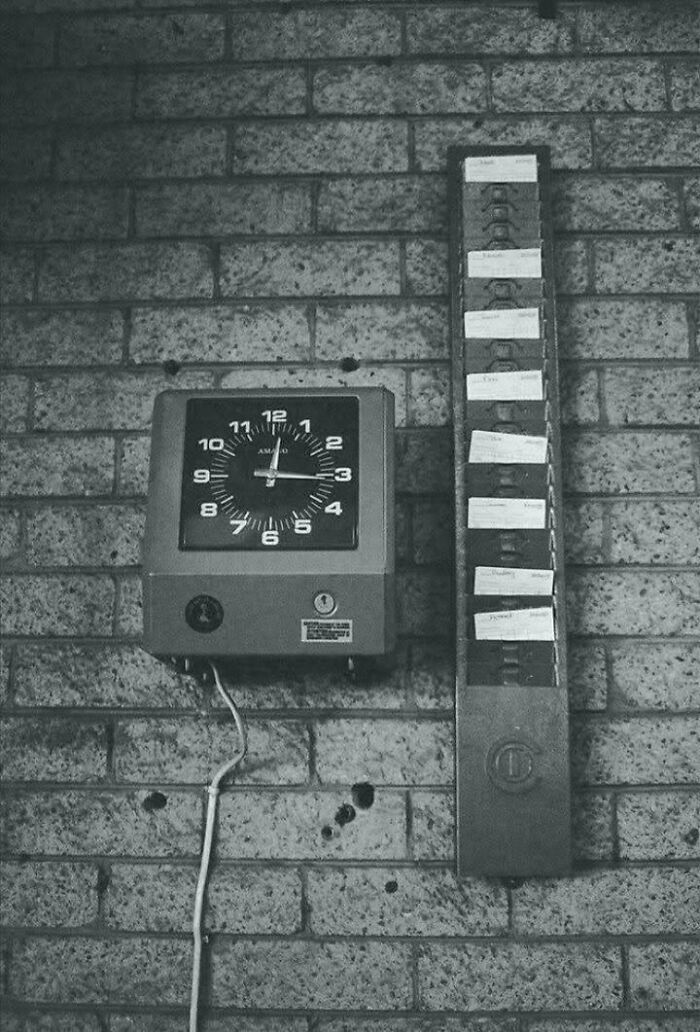 A black and white image of a time clock and a punch card rack on a brick wall, retro tech from the 80s.
