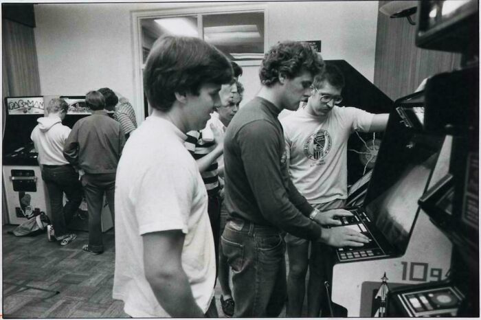 Several young men playing arcade games in the 80s, showcasing retro tech and gaming culture.