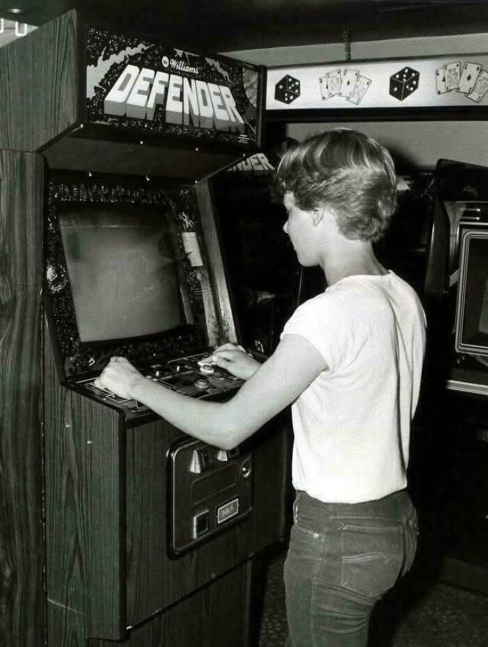 A person playing the Defender arcade game, an iconic piece of 80s retro tech, in a black and white photo.