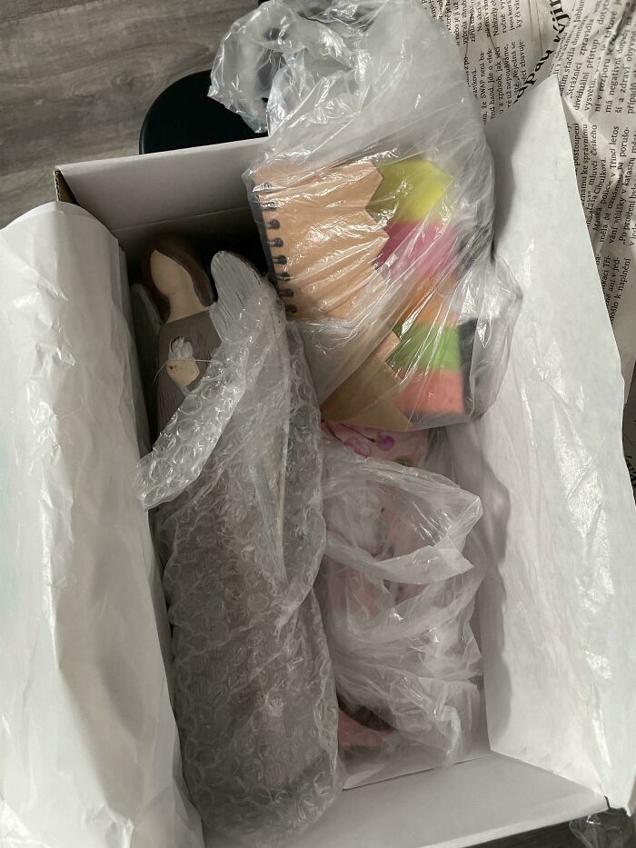 A box filled with various items, including an angel figurine and a colorful pencil, all wrapped in plastic for Vinted posts.