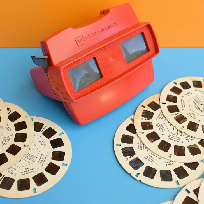 A vibrant red retro tech 3D View-Master with several classic reel discs.