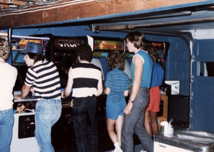 People playing arcade games, showcasing retro tech and the fun weirdness of the 80s.