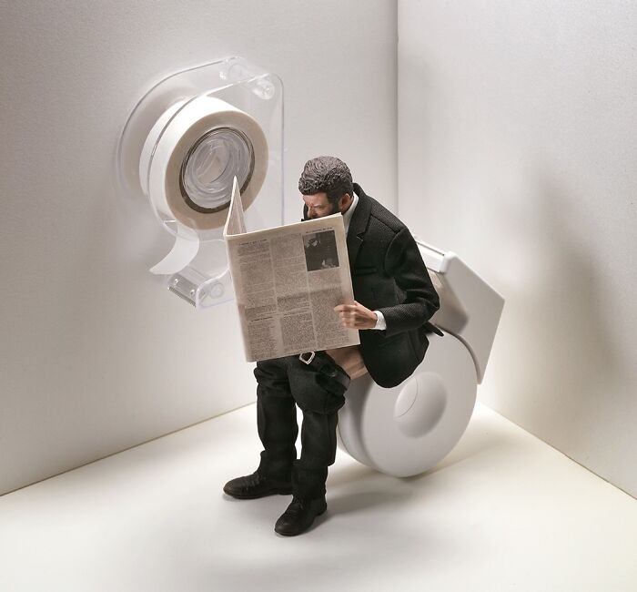 A miniature calendar scene by Tatsuya Tanaka features a figure on a toilet made of tape, reading a newspaper.