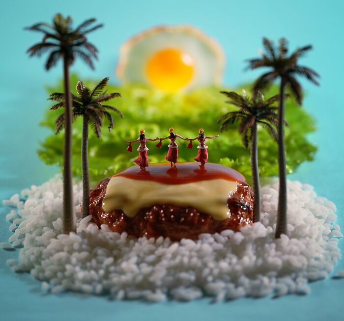 A miniature calendar work by Tatsuya Tanaka, showing hula dancers on a hamburger patty island with palm trees.