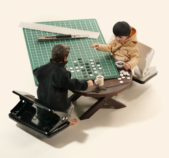 Tatsuya Tanaka miniature calendar work: Two miniature figures playing a board game on a cutting mat with office supplies.