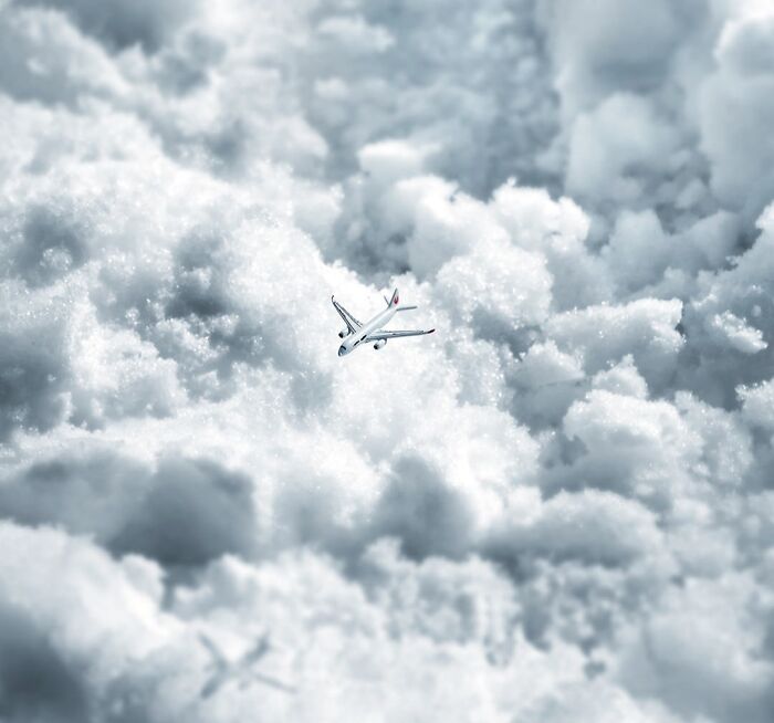 Miniature calendar scene by Tatsuya Tanaka showing a small airplane flying through cotton-like clouds.