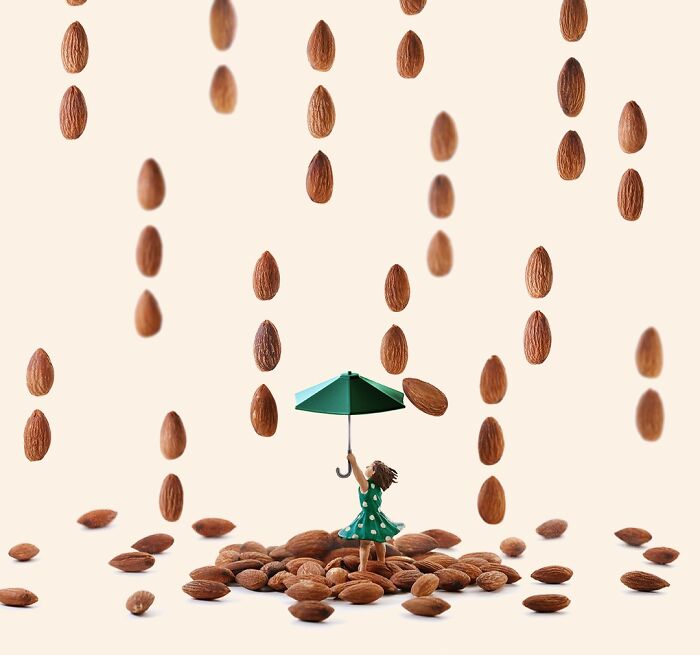 A Tatsuya Tanaka miniature calendar scene depicts a tiny figure holding an umbrella under falling almonds.