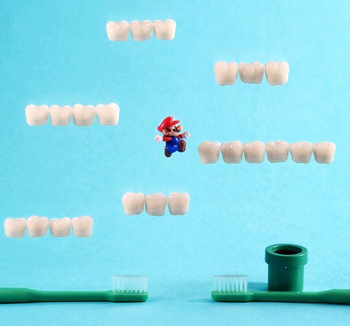 Tatsuya Tanaka miniature calendar work: Mario jumping on dental molds, toothbrushes below, on a blue background.