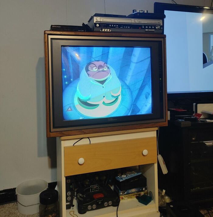 A CRT TV displaying an animated film, surrounded by retro tech including a VCR and game console.