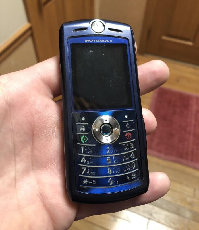A hand holding a blue Motorola flip phone, showcasing retro tech from the 80s in all its glorious weirdness.