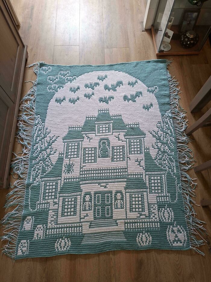 Crochet blanket on floor with haunted house and flying bats design