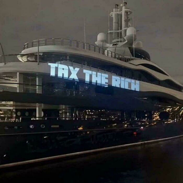 A luxury yacht with 'TAX THE RICH' projected onto its side, illustrating an 'Eat The Rich' moment.