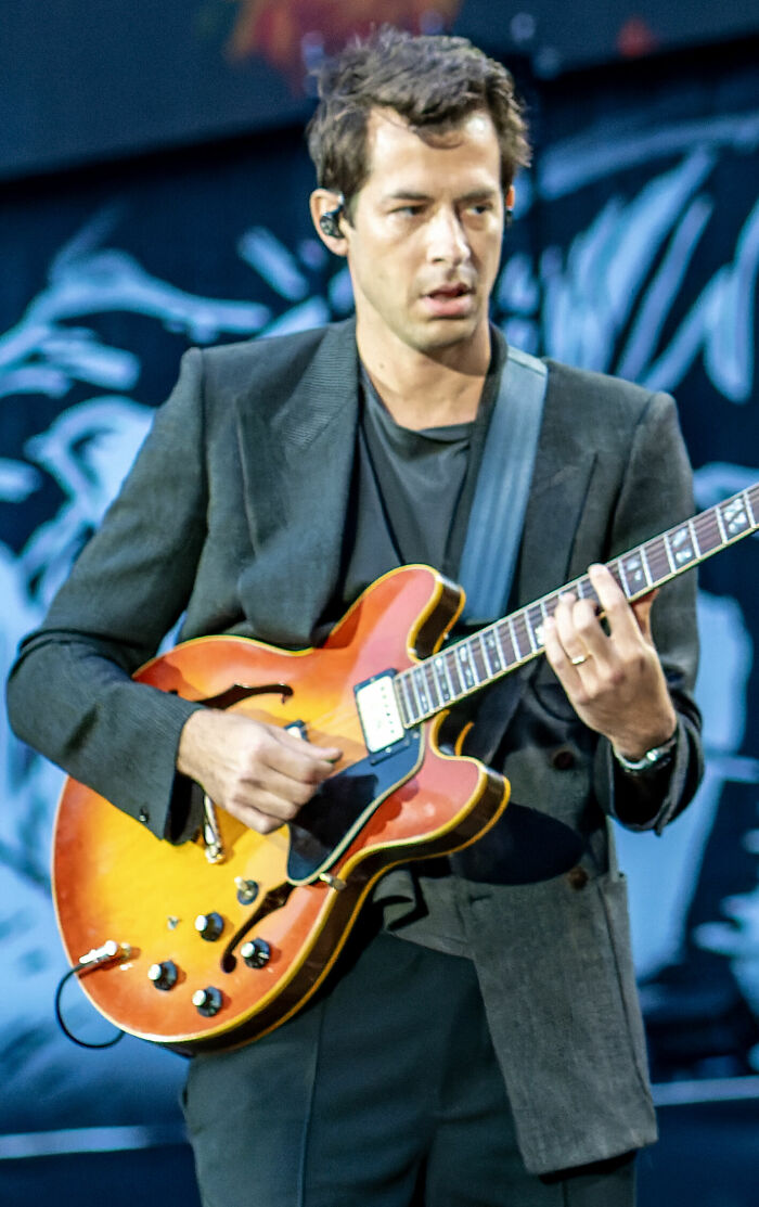 Mark Ronson performing live, playing a semi-hollow body electric guitar on stage.