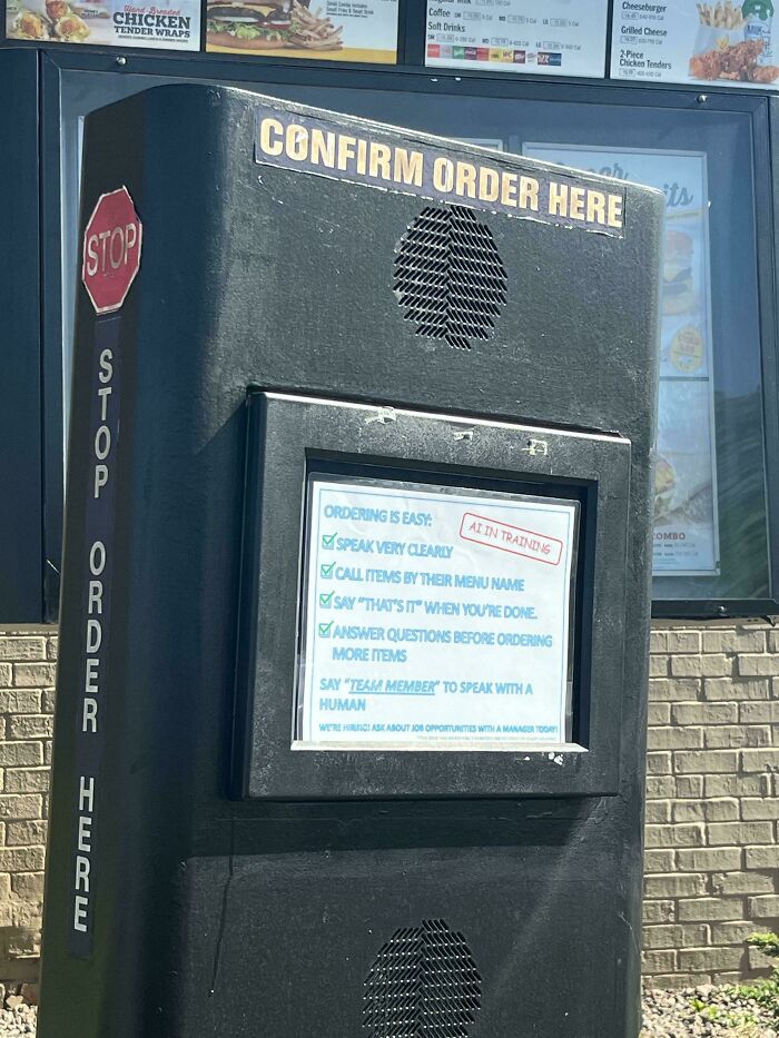 A close-up of a fast-food drive-thru menu featuring an AI in training notice, highlighting the sad world.