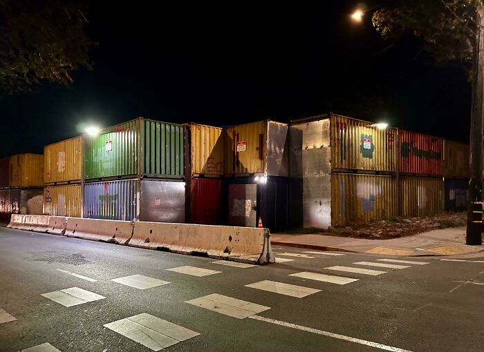 Stacked shipping containers at night with concrete barriers, representing the horrid and sad world.