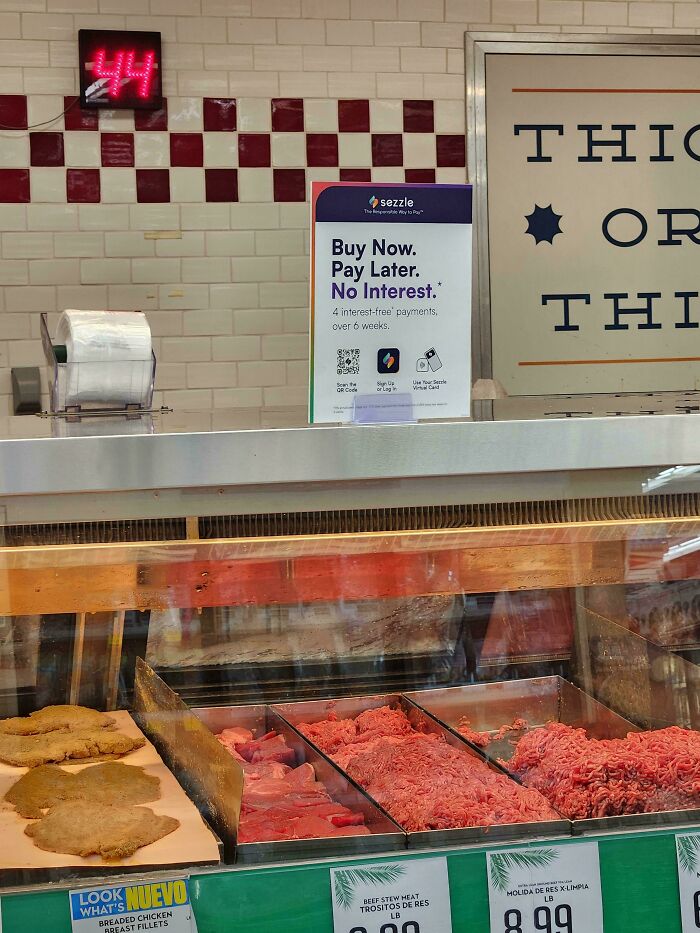 A grocery store meat counter with a sign for Buy Now, Pay Later, illustrating a sad world reality.
