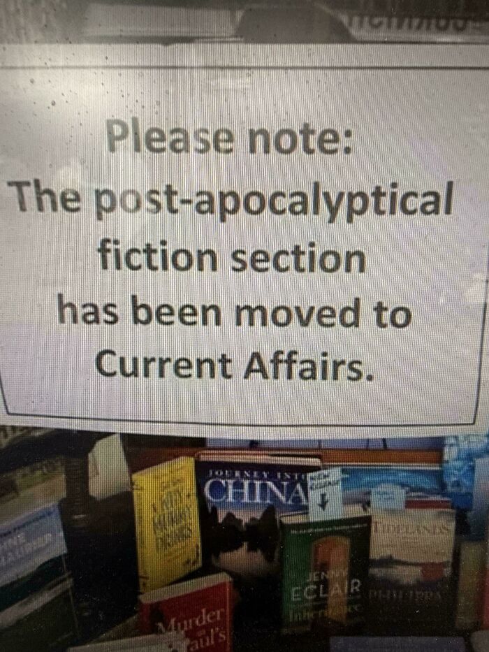 A sign stating the post-apocalyptic fiction section moved to Current Affairs, reflecting a horrid world view.