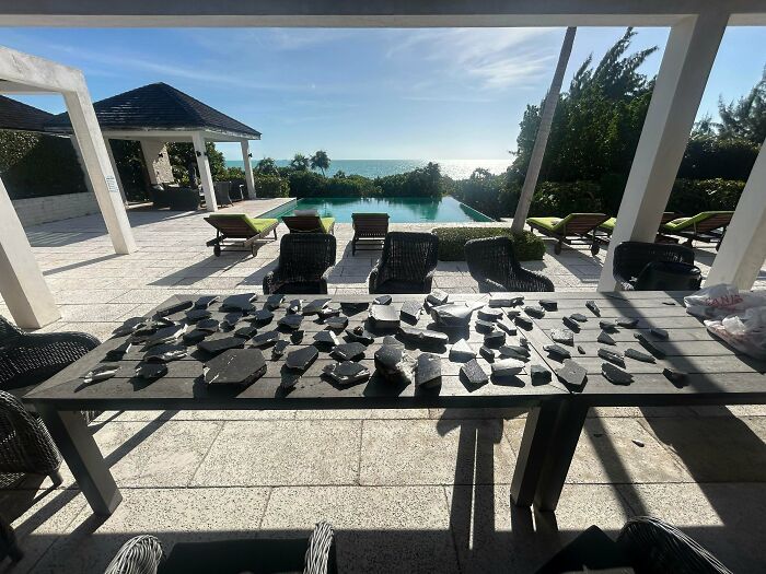 A wide view of a luxurious outdoor patio with a pool and ocean view, displaying numerous black stones on a table, representing the horrid world.