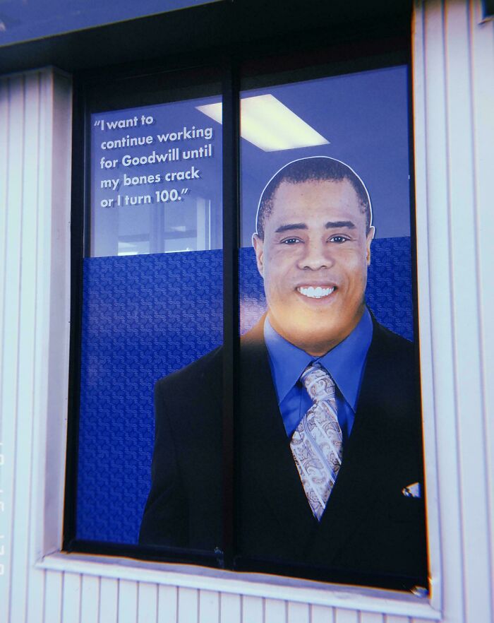 A window decal with a smiling man and a quote about working for Goodwill, showing aspects of a horrid world.