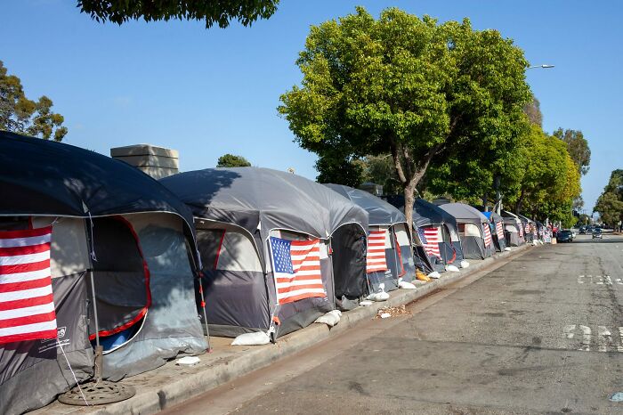 Row of tents with American flags along a street, depicting a horrid and sad world of homelessness.