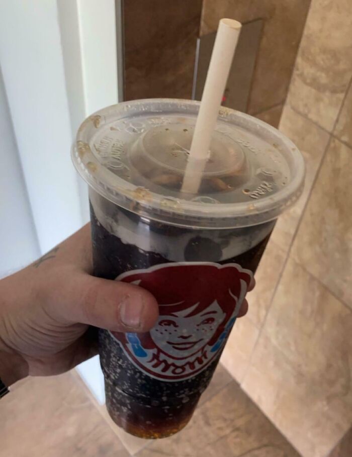 A hand holding a Wendy's soda cup, showing a horrid and sad world.