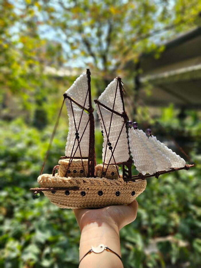 Hand holding a crochet sailboat with white sails and yarn details outdoors