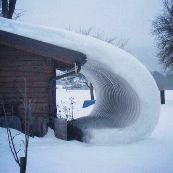 A baffling image of a thick layer of snow curved perfectly off a roof, making no physical sense.