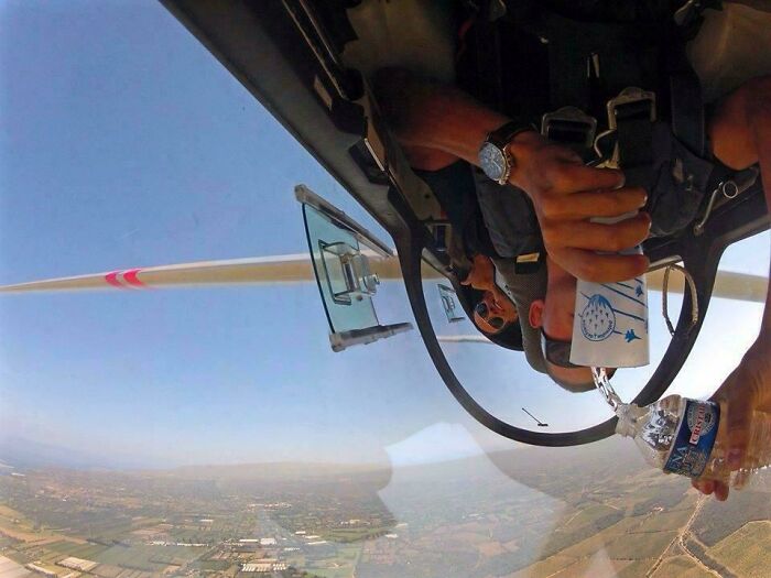 A baffling image of a person upside down in a plane, pouring water upwards, defying physical sense.