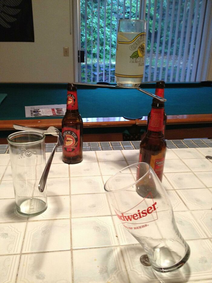 A baffling image of a glass and spoons precariously balanced on beer bottles, making no physical sense.