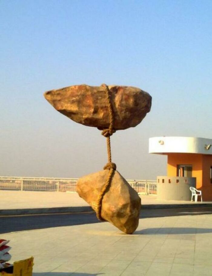 A baffling image of two large rocks suspended by a rope, seemingly defying physical sense in an outdoor setting.