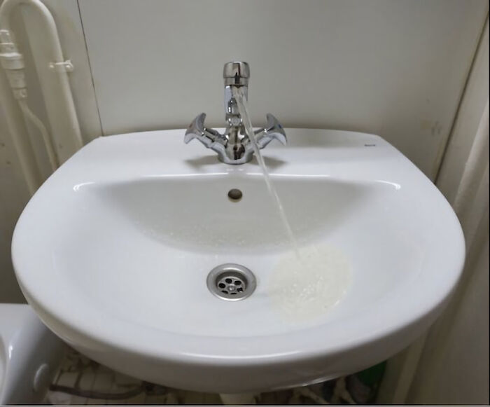 Water inexplicably flowing upwards from a sink drain, a baffling image that seems to make no physical sense.