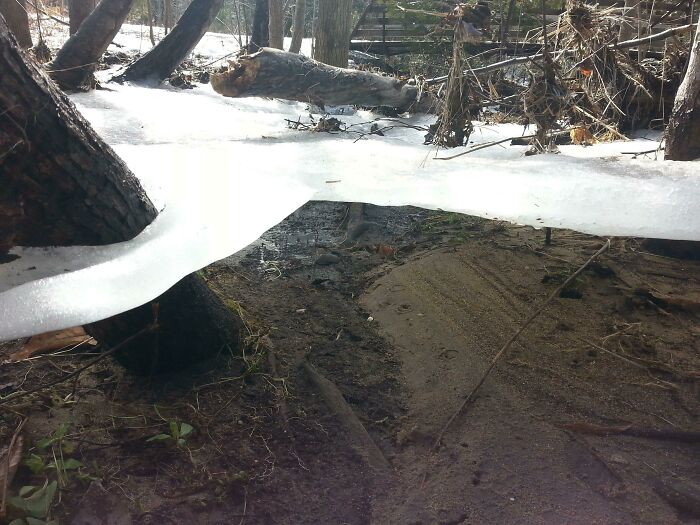 An image showing snow and ice creating a baffling illusion over a muddy bank, making no physical sense.