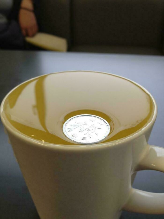 A baffling image of a coin floating on top of a drink in a cup, appearing to make no physical sense.