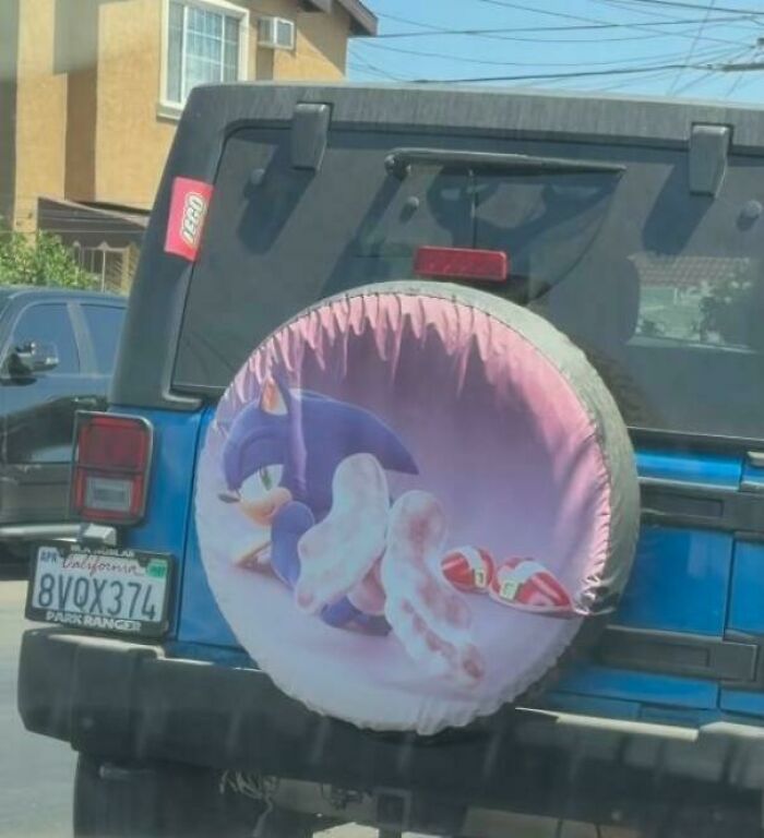 A blue Jeep with a cringey spare tire cover featuring Sonic the Hedgehog in a suggestive pose.