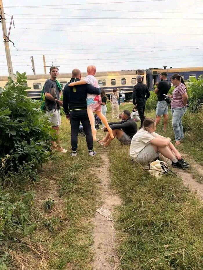 A man holding a mannequin leg on a grassy path near a train, surrounded by people, showcasing cringey situations.