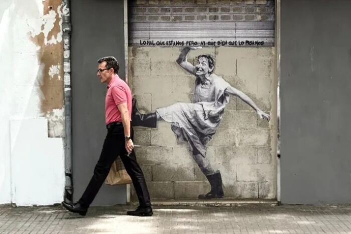 A street photographer captures an odd scene: a man walking past a graffiti of a woman with a kicking leg.