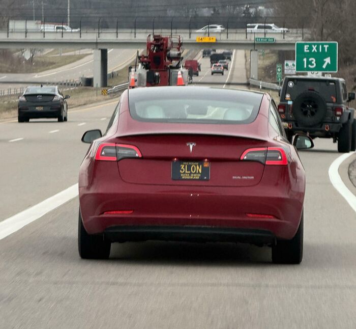A red Tesla on a highway with a vanity plate, an example of cringey people.