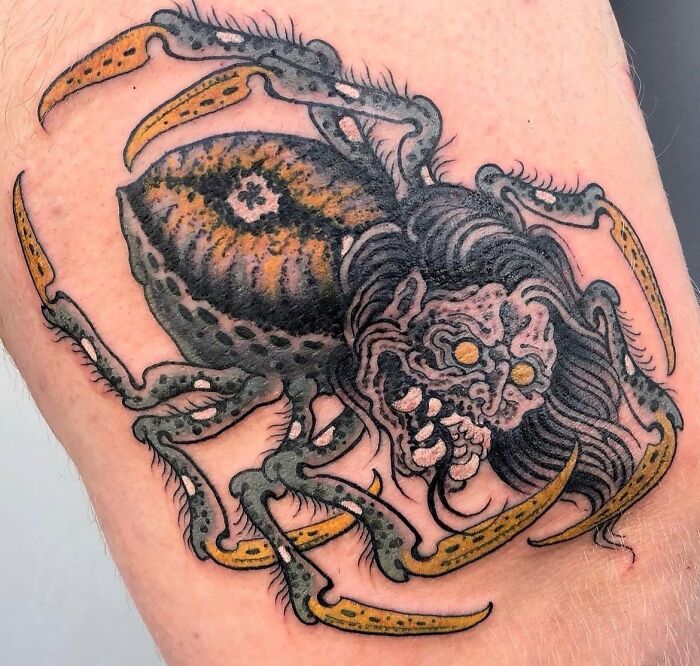 A vibrant ancient mythology tattoo featuring a spider creature with a monster head on skin.