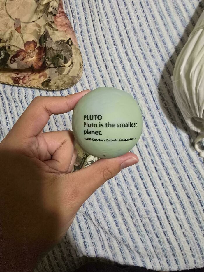A hand holding a stress ball stating Pluto is the smallest planet, a belief that has aged badly.